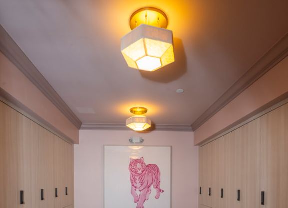A long bench with a wooden X base sits in a room with a pink painting on the wall.
