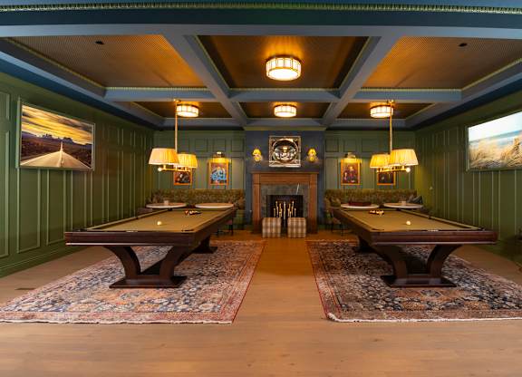 A room with two pool tables and a fireplace.