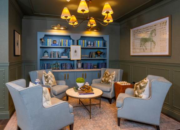 A living room with a grey sofa, two armchairs, a coffee table, and a bookshelf with books and decorative items.