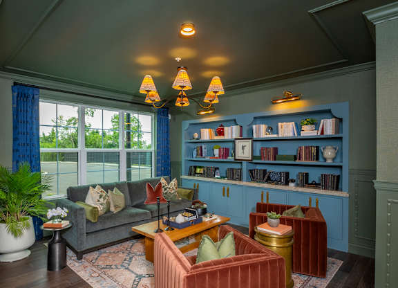 A living room with a grey couch, a red armchair, a wooden coffee table, and a bookshelf with books and decorative items.