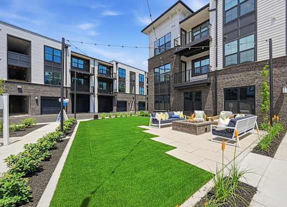 A modern courtyard with a grassy area and benches surrounded by buildings.