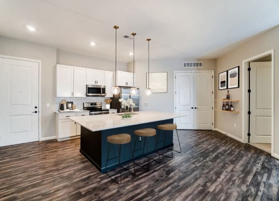 a kitchen with white cabinets and a blue island with three stools at Essex, Columbus, OH