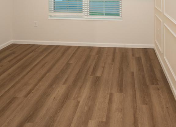 A room with a window covered by white blinds and wooden flooring.