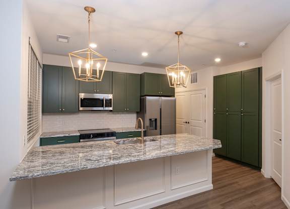 A kitchen with green cabinets and a marble countertop.