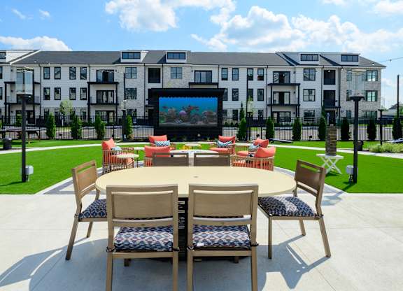 A table with chairs is set up in front of a building with a screen on it.
