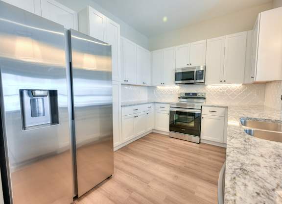 A modern kitchen with a stainless steel refrigerator and wooden flooring.