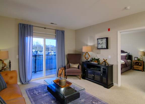 A living room with a brown couch, a coffee table, and a large window with curtains.