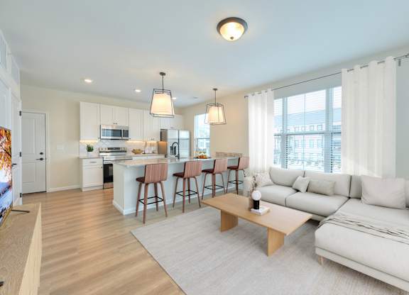 A well-lit, modern living room with a kitchen in the background.
