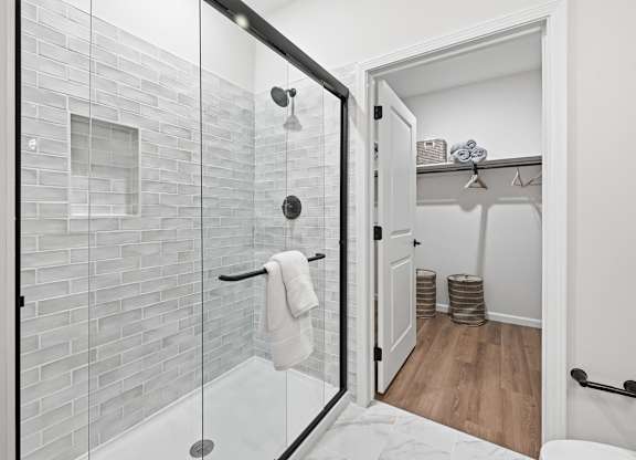 A white bathroom with a glass shower door and a white towel hanging on the shower rod.