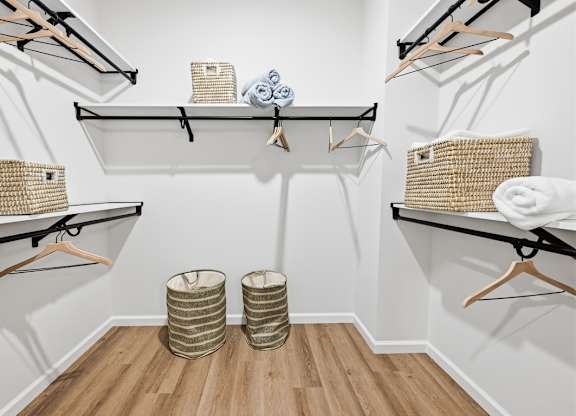 A white bathroom with a wooden floor and three shelves with baskets and towels.