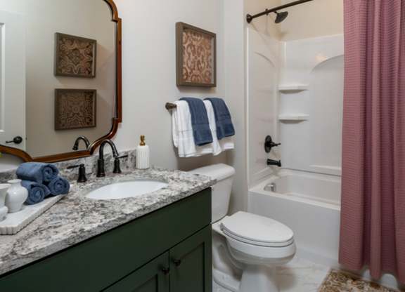 A bathroom with a sink, mirror, toilet, and shower.