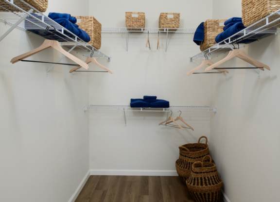 A room with a white wall and a wooden floor with clothes hanging on a rack.