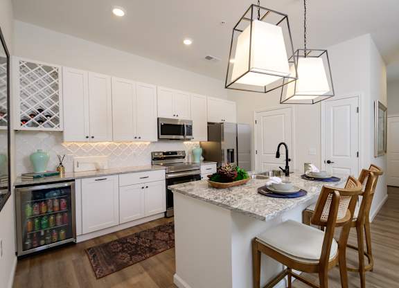 A kitchen with a white counter top and wooden chairs.