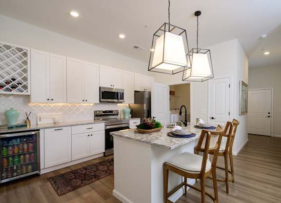 A kitchen with white cabinets and a central island with a marble top.