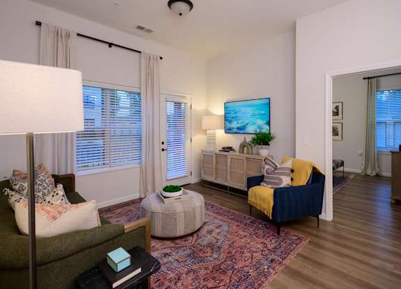 A living room with a green couch, a white lamp, a TV on the wall, and a rug on the floor.