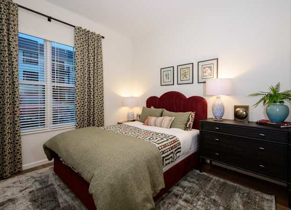 A bedroom with a bed, nightstand, and a window with curtains.