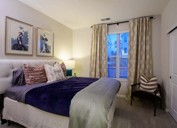 A bedroom with a bed, a chair, and two framed pictures on the wall with window  at Fairmont Apartments, Westerville, 43081