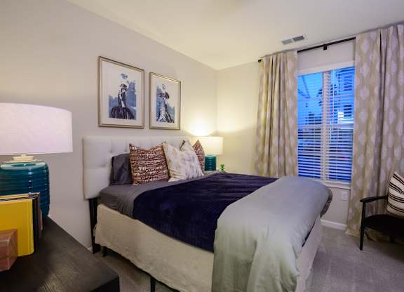 A bedroom with a bed, a chair, and two framed pictures on the wall. at Fairmont Apartments, Westerville