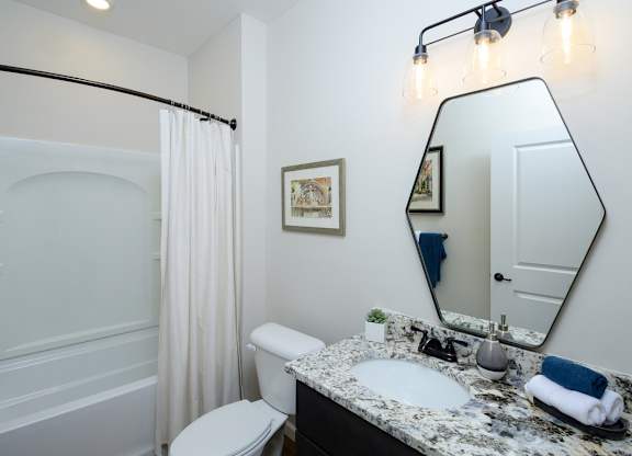 A bathroom with a white toilet, a sink, a mirror, and a shower. at Fairmont Apartments, Westerville