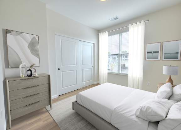 A person is lying on a bed in a bedroom with a white bedspread and a grey headboard.