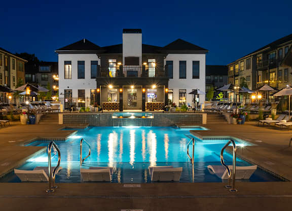 A large white building with a pool in front of it at night.