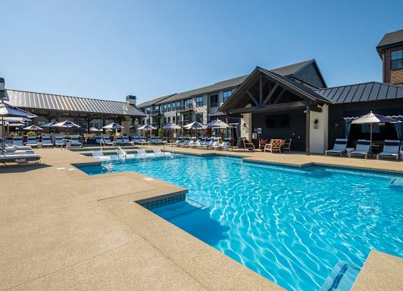 A large outdoor swimming pool with a patio area and lounge chairs.