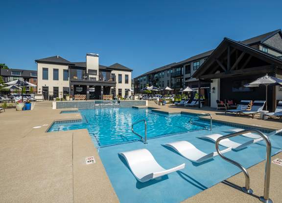 A large swimming pool with white lounge chairs and a building in the background.