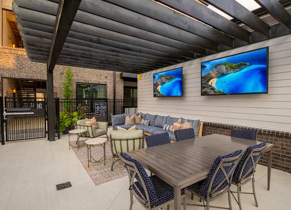 A patio with a table, chairs, and two TVs mounted on the wall.