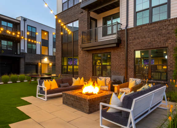 A patio with a fire pit and seating area in front of a modern building.