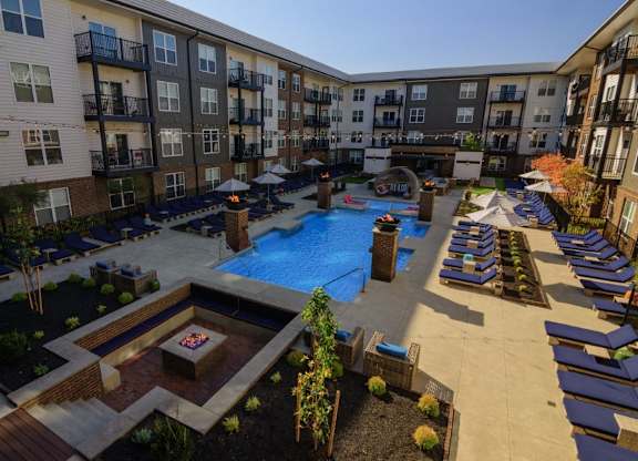 A large outdoor pool area with lounge chairs and a fire pit surrounded by apartment buildings.