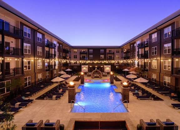A swimming pool surrounded by lounge chairs and balconies with lights strung up.