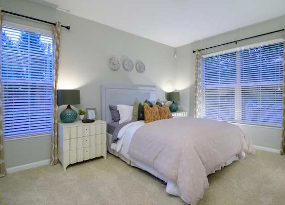 A bedroom with a bed, nightstand, and window with curtains.