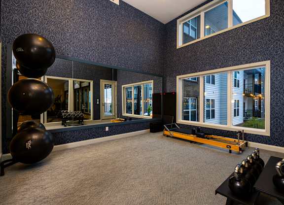 A gym with a mirror, a row of windows, and a row of exercise balls.