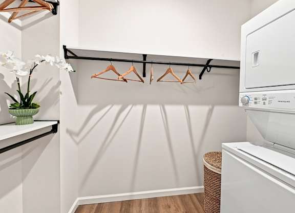 A white washing machine in a laundry room with a white wall and a white shelf.