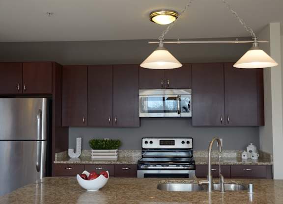 A kitchen with brown cabinets and a granite countertop at Cornerstone & Ravenna* Apartments, Shorewood, WI, 53211