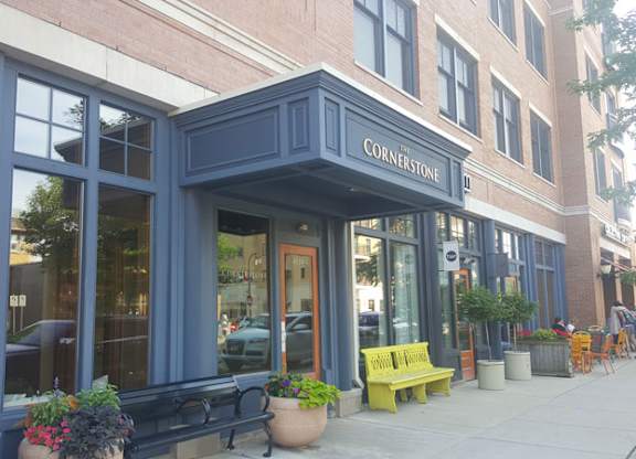 A storefront with a blue awning and a yellow bench in front at Cornerstone & Ravenna* Apartments, Shorewood 53211