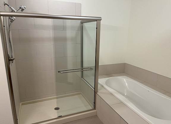 A white bathtub sits next to a glass shower door at Cornerstone & Ravenna* Apartments, Shorewood, Wisconsin