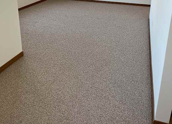 A room with a carpeted floor and a window with blinds at Cornerstone & Ravenna* Apartments, Shorewood 53211
