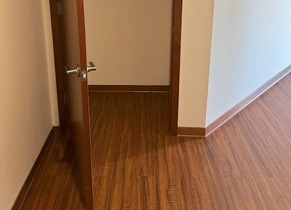 A wooden closet with a door open and clothes hanging inside at Cornerstone & Ravenna* Apartments, Wisconsin, 53211