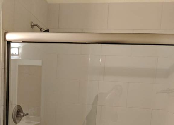 A white tiled shower with a glass door at Cornerstone & Ravenna* Apartments, Wisconsin