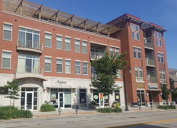 A red brick building with a white awning and a tree in front at Cornerstone & Ravenna* Apartments, Wisconsin