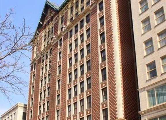 A tall red brick building with many windows stands next to a smaller building.