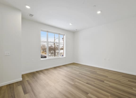 a living room with white walls and wooden floors and a window