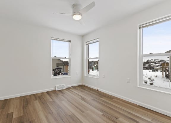 an empty living room with wood floors and three windows