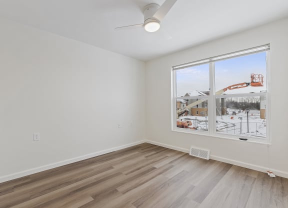 an empty living room with a large window and hardwood floors