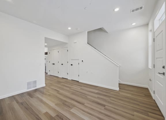 a living room with white walls and wooden floors and a staircase