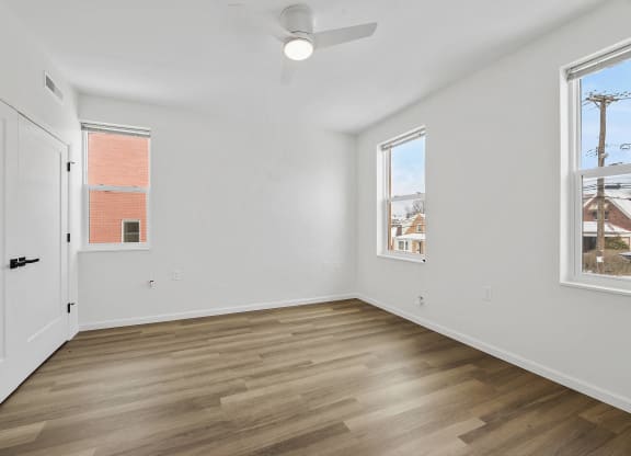a living room with white walls and wood flooring and a white door and windows