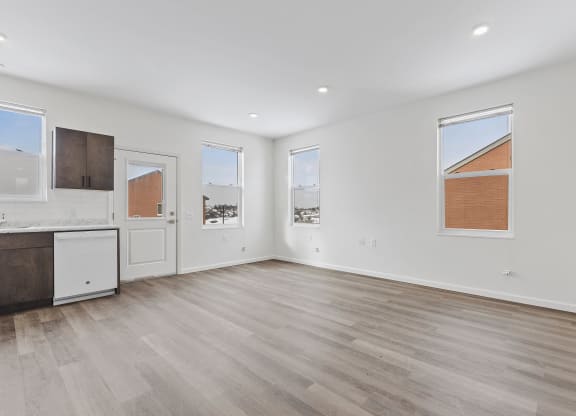 a living room with white walls and wood floors and a kitchen