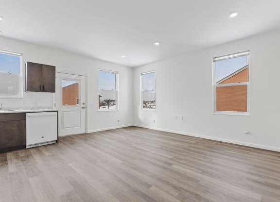 a living room with white walls and wood floors and a kitchen