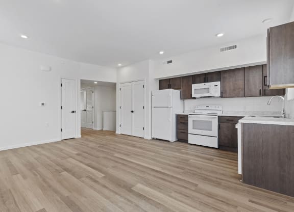 an empty kitchen with white appliances and wooden floors